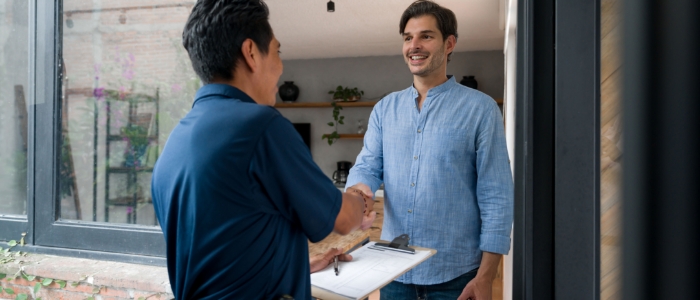 Man in blue shirt answers door and shakes technician in blue polos hand